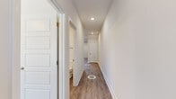 This two-story home offers a clean, modern aesthetic throughout, with consistent wood-look luxury vinyl plank flooring, neutral warm-toned walls, and recessed lighting found across both levels. The main floor provides an open-concept living and kitchen area, where white shaker-style cabinetry, a subway tile backsplash, stainless steel appliances, and a center island with pendant lighting create a functional and stylish culinary space. A carpeted staircase with a wood handrail and black balusters connects the two floors. The upper level houses the majority of the bedrooms, each featuring ceiling fans, generous windows that allow natural light and neighborhood views, and ample closet space — including double closets in select rooms. The primary bedroom includes a dedicated closet area. Hallways on both floors are bright and well-lit with recessed ceiling fixtures, maintaining a clean and open feel between rooms. The three bathrooms are finished with white tub-shower surrounds, brushed nickel fixtures, light tile flooring, and dark wood vanities topped with white countertops. A dedicated closet provides additional storage. The home's design prioritizes a cohesive, move-in-ready aesthetic with practical layouts throughout.