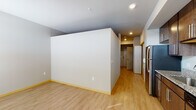 Located at 7920 Watts Rd in Madison, Wisconsin, this single-floor unit offers a clean, contemporary layout designed for comfortable everyday living. The kitchen serves as a functional centerpiece, showcasing rich dark-wood cabinetry, granite countertops, a stainless steel refrigerator, range, microwave, and dishwasher. Recessed lighting illuminates the space efficiently, while vertical blinds on a large window allow for adjustable natural light. Light hardwood-style flooring runs throughout the main living and kitchen areas, creating a cohesive and bright aesthetic. The open layout connects the kitchen to a generously sized living area, offering flexible arrangement possibilities. A ceiling fan is present in the living space, adding to everyday comfort. The bedroom area features carpeted flooring and a built-in closet with organized storage. The bathroom is finished with a dark-wood vanity, white countertop, a large wall mirror, granite-style tile flooring, and accessibility-friendly grab bars near the tub and toilet. Neutral wall tones and consistent trim details throughout the unit contribute to a calm, well-maintained atmosphere. The overall design balances practicality and modern finishes in a straightforward, livable floor plan.