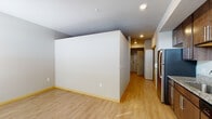 Located at 7920 Watts Rd in Madison, Wisconsin, this single-floor unit offers a clean, contemporary layout designed for comfortable everyday living. The kitchen serves as a functional centerpiece, showcasing rich dark-wood cabinetry, granite countertops, a stainless steel refrigerator, range, microwave, and dishwasher. Recessed lighting illuminates the space efficiently, while vertical blinds on a large window allow for adjustable natural light. Light hardwood-style flooring runs throughout the main living and kitchen areas, creating a cohesive and bright aesthetic. The open layout connects the kitchen to a generously sized living area, offering flexible arrangement possibilities. A ceiling fan is present in the living space, adding to everyday comfort. The bedroom area features carpeted flooring and a built-in closet with organized storage. The bathroom is finished with a dark-wood vanity, white countertop, a large wall mirror, granite-style tile flooring, and accessibility-friendly grab bars near the tub and toilet. Neutral wall tones and consistent trim details throughout the unit contribute to a calm, well-maintained atmosphere. The overall design balances practicality and modern finishes in a straightforward, livable floor plan.