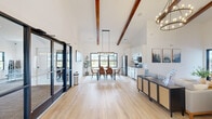 Located at 307 Willow Manor Dr in O'Fallon, Missouri, this single-floor community space delivers a striking blend of modern farmhouse aesthetics and functional design. The open-concept layout connects the living room, dining area, and kitchen seamlessly, all unified by wide-plank light hardwood flooring and crisp white walls that amplify the sense of space and airiness throughout.

Soaring vaulted ceilings with prominent exposed dark wood beams serve as the architectural centerpiece, lending warmth and dramatic height to the interior. The living room is bright and welcoming, featuring a stone fireplace with a reclaimed wood mantel and large glass entry doors that invite natural light while offering views to the outdoors.

The dining area is anchored by a rectangular wood table surrounded by cognac leather chairs, topped with a statement linear chandelier. Large black-framed windows frame outdoor views and flood the space with natural light. Adjacent, the kitchen is outfitted with tall white shaker cabinetry, stainless steel appliances, light quartz countertops, and matte black hardware for a clean, contemporary finish.

A glass-paneled wall and door provide a transparent connection to a fitness area visible from the main space. The entry foyer features stylish pendant lighting and planters, creating an inviting arrival experience. Throughout, the design balances modern sophistication with approachable warmth.