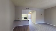 This single-floor unit is designed with a practical, open layout that maximizes the available living space. The main living and dining area features light-toned laminate wood flooring that extends throughout much of the unit, neutral gray walls, and a textured ceiling. A large window fitted with vertical blinds allows natural light to fill the space, while a doorway connects seamlessly to the adjoining room, enhancing the open feel.

The kitchen is accessible via a pass-through counter with an overhang that doubles as a breakfast bar, offering a casual dining option. Inside, the kitchen is equipped with white cabinetry, gray laminate countertops, a stainless steel sink, and black appliances including a refrigerator, electric range, and oven. Light laminate flooring continues throughout this space.

The bedroom is a well-proportioned room with the same neutral color palette, laminate flooring, vertical blinds, a ceiling fan, and a closet, providing ample storage.

The bathroom features a single-sink vanity with white cabinetry and gray countertop, a wall-mounted mirror, and a combined tub and shower. Light wood-style flooring ties the space together, maintaining the unit's cohesive, clean aesthetic throughout.