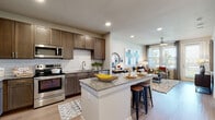 Located at 13003 FM-1488 in Magnolia, Texas, this single-floor residence offers a well-designed open-concept layout that seamlessly connects the kitchen, dining, and living areas. The kitchen is a standout feature, showcasing rich warm-toned cabinetry, a classic white subway tile backsplash, granite countertops, and a full suite of stainless steel appliances including a refrigerator, range, microwave, and dishwasher. A central island with granite counters and bar seating provides additional prep space and a casual dining option, making it both functional and inviting.

The living area flows naturally from the kitchen, bathed in natural light from large windows dressed with sheer curtains and blinds. A ceiling fan adds comfort, while the outdoor views lend a pleasant sense of connection to the surrounding environment. Light wood-style flooring runs throughout the main living spaces, contributing to a clean, contemporary aesthetic.

The bedroom is generously sized, featuring large windows that bring in abundant natural light and views of the outdoors. A ceiling fan adds to the room's comfort. The adjacent bathroom includes dark cabinetry with granite countertops, wood-style flooring, and subway tile detailing in the shower area, maintaining the consistent, polished design found throughout the residence.