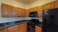 This ground-floor unit offers a thoughtfully designed single-level layout accommodating three bedrooms and two full bathrooms. The living room serves as the focal point of the home, featuring a tile-surround fireplace flanked by built-in cabinetry with dark countertops and windows on either side, flooding the space with natural light. A ceiling fan overhead and plush wall-to-wall carpeting contribute to a comfortable atmosphere. An adjacent area provides additional living or dining space, accented by a chandelier and direct access to other areas of the home.

The kitchen is well-equipped with warm oak cabinetry extending to the ceiling, dark granite-style countertops, tile flooring, and black appliances including a range, over-the-range microwave, and refrigerator. Each of the three bedrooms features soft carpeting, a ceiling fan with light fixture, and windows that bring in natural light. The two bathrooms are finished with light tile flooring; one includes a vanity with ample storage and a large mirror, while the other features a full tub-shower combination with clean white tile surround.