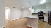 This single-floor residence offers a thoughtfully designed open-concept layout that seamlessly connects the kitchen and living area. The kitchen is a functional highlight, featuring stainless steel appliances including a refrigerator, range, and microwave, complemented by white shaker cabinetry, a tile backsplash, and a peninsula with a white quartz countertop and pendant lighting above. The living area flows naturally from the kitchen, finished with warm hardwood-style flooring, crown molding, and a ceiling fan, with windows allowing natural light to fill the space. The entry foyer offers a charming arched built-in shelving nook, adding character at the threshold of the home. The bedrooms are well-proportioned, each featuring the same hardwood-style flooring, ceiling fans, and windows with blinds that bring in natural light. The bathroom is finished with warm beige tile surrounding a full soaking tub, a white vanity with quartz countertops, and gold-toned hardware accents. Throughout the residence, a neutral color palette and clean finishes create a cohesive, modern ambiance that is both inviting and move-in ready.