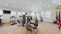 Located at 1300 South Park Way in Sanford, North Carolina, this fitness center is a single-floor facility designed to support a wide range of workout routines. The space is divided into distinct exercise zones, each thoughtfully arranged to maximize functionality and flow.

The main strength training area features vaulted ceilings that lend an open, airy feel, complemented by recessed lighting and full-length mirrored walls that visually expand the space and allow users to monitor their form. This section is equipped with a cable machine, a multi-functional power rack, and multiple dedicated strength machines, alongside a well-stocked dumbbell rack with kettlebells and weight plates.

A separate cardio zone is lined with large, white-trimmed windows that invite ample natural light and offer views of the surrounding community. This area houses treadmills, ellipticals, and stationary bikes, including a recumbent cycle, all positioned to take advantage of the bright, welcoming atmosphere.

Throughout the facility, durable carpet tile flooring provides both comfort and traction. The clean white walls and consistent recessed lighting maintain a crisp, professional aesthetic. The layout offers generous open floor space between equipment, ensuring ease of movement. This fitness center provides residents with a comprehensive, well-maintained environment suited for both cardio and strength training goals.