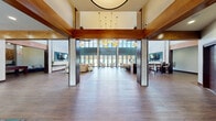 Located at 1715 Lake Michigan Dr in Valparaiso, Indiana, this impressive single-floor amenity space offers a thoughtfully designed environment that balances elegance with functionality. The layout spans a generous footprint, anchored by soaring ceilings that create a dramatic sense of openness throughout.

The grand lobby entrance features rich wood-look flooring, exposed wooden beam accents, and a statement pendant light fixture, setting an upscale tone from the moment of arrival. Sleek elevator doors and floor-to-ceiling windows flood the entry with natural light and provide views of the surrounding outdoor areas.

Two distinct living rooms serve different purposes. The primary lounge is a showpiece, boasting two stories of floor-to-ceiling glass panels that bathe the space in natural light and offer sweeping outdoor views. Comfortable seating arrangements in neutral, patterned upholstery are positioned throughout. The secondary living area includes a wall-mounted flat-screen TV, warm textured wall panels, and an adjacent game room complete with a pool table and mosaic tile accent wall beneath exposed beam ceilings.

A dedicated business center provides workstations, comfortable seating, and ample natural light through multiple windows. The space also features a kitchenette and bar-height seating area beneath a dramatic circular ceiling detail with cascading pendant lights. Rich hardwood-style flooring and warm wood trim details unify the entire space cohesively.