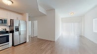 This single-floor unit offers a clean, contemporary design throughout. The open-concept living and dining area is characterized by crisp white walls, light wood-tone laminate flooring, and generous natural light streaming in through large sliding glass doors fitted with vertical blinds, creating an airy, welcoming atmosphere.

The kitchen is well-equipped with a full suite of stainless steel appliances, including a side-by-side refrigerator with ice and water dispenser, electric range, over-the-range microwave, and dishwasher. White shaker-style cabinetry pairs with dark granite countertops to create a polished, functional workspace. The kitchen flows naturally into the main living area via a hallway corridor.

Multiple bedrooms feature the same light wood-tone flooring and neutral white walls, each benefiting from natural light provided by horizontal blinds-fitted windows. The rooms offer versatile, adaptable layouts.

Two bathrooms serve the unit. One features large-format gray stone-look wall tiles surrounding a soaking tub and shower combination, while the second bathroom includes a dedicated walk-in shower with matching tile surround and a white base pan with chrome fixtures. Both bathrooms include tile flooring consistent with their respective designs, maintaining a cohesive, modern aesthetic throughout the unit.