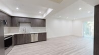 Located at 11117 Hartsook St in the North Hollywood neighborhood of Los Angeles, this single-floor unit showcases a clean, contemporary design with high-quality finishes throughout. The open-concept layout is anchored by light-toned hardwood-style flooring that runs seamlessly across the living and kitchen areas, creating a cohesive and airy feel.

The kitchen is a standout feature, equipped with dark wood-grain cabinetry accented by sleek brushed-nickel hardware, white quartz countertops, and a full suite of stainless steel appliances including a side-by-side refrigerator, range, over-the-range microwave, and dishwasher. A subway tile backsplash adds a refined touch, while recessed lighting set within a tray ceiling enhances the modern aesthetic.

The living area is generously proportioned, with crisp white walls and recessed lighting that keep the space bright and versatile. A gated exterior door allows access to a lush outdoor area, bringing in natural light and a connection to the outside.

The bathroom is finished with large-format marble-look tile flooring, a dark wood-grain vanity with white countertop, an oversized wall mirror, and a tiled shower-tub combination enclosed by a glass door — all contributing to a polished, spa-like atmosphere. The unit's consistent use of dark cabinetry against white surfaces and light flooring creates a balanced, modern look throughout.
