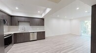 Located at 11117 Hartsook St in the North Hollywood neighborhood of Los Angeles, this single-floor unit showcases a clean, contemporary design with high-quality finishes throughout. The open-concept layout is anchored by light-toned hardwood-style flooring that runs seamlessly across the living and kitchen areas, creating a cohesive and airy feel.

The kitchen is a standout feature, equipped with dark wood-grain cabinetry accented by sleek brushed-nickel hardware, white quartz countertops, and a full suite of stainless steel appliances including a side-by-side refrigerator, range, over-the-range microwave, and dishwasher. A subway tile backsplash adds a refined touch, while recessed lighting set within a tray ceiling enhances the modern aesthetic.

The living area is generously proportioned, with crisp white walls and recessed lighting that keep the space bright and versatile. A gated exterior door allows access to a lush outdoor area, bringing in natural light and a connection to the outside.

The bathroom is finished with large-format marble-look tile flooring, a dark wood-grain vanity with white countertop, an oversized wall mirror, and a tiled shower-tub combination enclosed by a glass door — all contributing to a polished, spa-like atmosphere. The unit's consistent use of dark cabinetry against white surfaces and light flooring creates a balanced, modern look throughout.