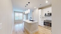 Located at 750 W Grand Pkwy S in Katy, TX, this thoughtfully designed two-bedroom, two-bathroom home offers a clean, modern aesthetic across a single floor. The open-concept kitchen and living area serves as the heart of the home, showcasing crisp white shaker cabinetry with matte black hardware, a large center island with a white quartz countertop, an undermount sink, and a suite of stainless steel appliances including a French door refrigerator, range with microwave, and dishwasher. Light wood-tone flooring and pendant lighting complete the polished look. The spacious primary bedroom features plush carpet, a ceiling fan, and multiple windows that invite generous natural light and neighborhood views, along with direct access to a closet and an en-suite bathroom. The second bedroom also offers carpeted flooring and a bright window. Both bathrooms are finished with white vanities, quartz countertops, matte black fixtures, and tub-shower combinations adorned with marble-style tile surrounds. Additional living areas feature light wood flooring and exterior door access, enhancing the airy, connected feel of the home. Neutral tones and contemporary finishes create a cohesive, move-in-ready atmosphere throughout.
