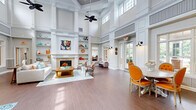 Located at 101 Sabal Palm Ln in Chesapeake, Virginia, this single-story clubhouse facility at MAA Adalay Bay offers a thoughtfully designed community space spanning a generous footprint. The centerpiece of the facility is a dramatic main living area boasting soaring double-height ceilings, intricate wainscoting, and rich hardwood flooring. Towering clerestory windows flood the space with an abundance of natural light, while a stately fireplace framed by built-in shelving serves as an elegant focal point. Ceiling fans complement the airy atmosphere throughout. A dining area with vibrant accent chairs and a round table sits adjacent to the main lounge, creating a seamless, open flow. A secondary living room features warm, intimate décor with bold terracotta walls, colorful artwork, and cozy seating arrangements. The hallway connects all areas efficiently, while a dedicated office space, finished with patterned carpeting and classic furnishings, provides a quiet professional environment. The fitness center is exceptionally well-equipped, featuring Matrix cable machines, free weights, treadmills, ellipticals, and stationary bikes beneath a vaulted ceiling with large windows overlooking the outdoors. Mirrored walls and rubber flooring complete this modern exercise space. Together, these amenity spaces deliver a welcoming, upscale community experience.