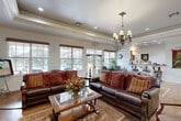 Located at 2118 W Old Spanish Trl in New Iberia, Louisiana, this single-floor community space exudes classic Southern charm through its thoughtfully curated interiors and refined architectural details. Polished stained concrete floors run throughout, complementing the ornate crown molding and tray ceilings adorned with elegant chandeliers and recessed lighting. A welcoming entry corridor lined with framed artwork and a wooden credenza sets the tone for the warm, traditional aesthetic found throughout. The main lounge area is anchored by rich leather sofas dressed with decorative throw pillows, arranged around a glass-top coffee table atop a patterned area rug. Large multi-pane windows and French doors flood the seating areas with natural light while offering views of the outdoor surroundings. A dedicated activity and gifts area provides a casual, functional space with organized display furnishings, art supply stations, and open access to adjoining rooms. A kitchen bar with counter-height seating, warm wood cabinetry, and a connected dining area with wrought-iron furniture adds to the versatility of the space. Throughout, vibrant tapestries, potted plants, and curated décor create an inviting, community-oriented ambiance rooted in the culture and hospitality of South Louisiana.