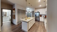 Located at 22415 Market St in Cornelius, NC, this well-appointed single-floor residence offers a thoughtfully designed layout with modern finishes throughout. The kitchen serves as a central highlight, boasting white shaker cabinetry, granite countertops, a subway tile backsplash, stainless steel appliances, and a central island with pendant lighting and bar seating — ideal for both cooking and casual dining. Wood-look flooring runs through the main living and kitchen areas, adding warmth and continuity. The living room provides a comfortable gathering space with room for generous seating and is accented by hardwood-style flooring and natural light. Multiple bedrooms feature plush carpeting, ceiling fans, and ample natural light from well-positioned windows. Each bedroom offers a calm, restful ambiance. The bathrooms are finished with granite-topped white vanities and wood-look tile flooring, with tub-shower combinations. Walk-in closet space provides practical wire-rack shelving for ample storage. The overall design strikes a balance between modern aesthetics and everyday functionality, making this Cornelius residence a comfortable and well-equipped home.
