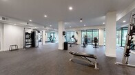 Located at 7510 N Oak Trafficway in Gladstone, Missouri, this fitness center offers a comprehensive, single-floor workout facility thoughtfully divided into two distinct training areas. The main workout floor is generously proportioned, featuring rubber sport flooring, recessed ceiling lighting, and structural columns that define the open layout without restricting movement. Floor-to-ceiling black-framed windows line one wall, flooding the cardio zone with natural light and providing refreshing views of the surrounding greenery — an inviting backdrop for treadmills, elliptical machines, and rowing equipment. Full-length mirrors along another wall visually expand the space and support proper form during strength training. A dedicated free weights area includes a squat rack with Olympic barbells and a dumbbell station, catering to a range of strength training needs. A separate, enclosed room serves as a functional training studio, outfitted with a heavy punching bag, medicine balls, kettlebells, TRX suspension trainers, and battle rope equipment — ideal for high-intensity and cross-training workouts. This room features carpet tile flooring and bright overhead lighting. Together, the two zones provide a well-rounded fitness environment suitable for cardio, strength, and functional training disciplines.
