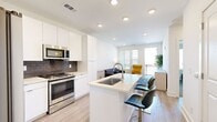 This thoughtfully designed one-bedroom, one-bathroom residence delivers a clean, contemporary aesthetic across a single floor. The open-concept kitchen flows seamlessly into the living area, anchored by a large island with a built-in sink, light quartz countertops, and bar seating for casual dining. The kitchen is outfitted with stainless steel appliances — including a refrigerator, range, microwave, and dishwasher — complemented by crisp white cabinetry and a navy blue subway tile backsplash. Light wood-look flooring ties the kitchen and living spaces together. The living room is bright and welcoming, featuring large windows with blinds that allow generous natural light, and a door leading out to a private balcony. The bedroom offers comfortable carpeting, a ceiling fan, and dual windows with urban views, creating a calm retreat. Adjacent to the bedroom is a well-appointed bathroom with wood-look tile flooring and a walk-in closet with built-in shelving that provides ample, organized storage. Throughout, the residence maintains a neutral, modern palette with recessed lighting, clean lines, and a cohesive design that maximizes the efficient use of space.