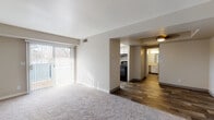Located at 390 E 4140 S in Salt Lake City, Utah, this single-story unit offers a well-organized layout with a thoughtful mix of flooring materials and natural light throughout. The living area is generously sized, featuring plush neutral carpeting, high ceilings, and a sliding glass door with vertical blinds that provides outdoor views and fills the space with natural light. A structural beam detail adds architectural character to the transition between living zones.

The kitchen is a functional galley-style space outfitted with white cabinetry, light stone-finish countertops, wood-look flooring, and black appliances including a range and refrigerator. A window above the counter allows natural light to brighten the workspace. Ample upper and lower cabinet storage ensures practical utility.

The bedroom features neutral carpet, a window with blinds for natural light, and clean, simple wall finishes, creating a calm and comfortable environment. The bathroom includes a vanity with matching stone-finish countertop and white cabinetry, wood-look flooring, and a separate toilet area, offering a clean, updated aesthetic. The overall ambiance of the unit is bright and neutral, with consistent finishes that create a cohesive, move-in-ready feel throughout.