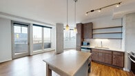 Located on the 14th floor at 811 S Washington Ave in downtown Minneapolis, this 2-bedroom, 2-bathroom residence offers a thoughtfully designed open-concept layout with modern finishes throughout. The kitchen and living area share a generous open floor plan, anchored by rich hardwood flooring and a distinctive exposed concrete column that adds an industrial character. The kitchen is well-equipped with stainless steel appliances, a gas range, a subway tile backsplash, warm wood cabinetry, open shelving, and a central island with pendant lighting — ideal for both cooking and entertaining. A glass door leads directly from the living area to a private balcony, flooding the space with natural light and offering sweeping views of the Minneapolis skyline. The primary bedroom features plush carpeting, a ceiling fan, large windows with city views, and access to a built-in shelved closet. The second bedroom includes a stylish barn-style sliding door. Both bathrooms are cleanly finished — one features large-format tile flooring with a wood-framed vanity mirror, while the other showcases a walk-in glass shower with classic white subway tile. The unit also includes a dedicated closet for additional storage.