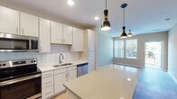 Located at 728 N Church St in Spartanburg, South Carolina, this single-floor residence offers a thoughtfully designed layout with contemporary finishes throughout. The kitchen serves as a standout centerpiece, showcasing white shaker-style cabinetry, a classic subway tile backsplash, and gleaming quartz countertops. A central island provides additional prep space and casual seating, while a full suite of stainless steel appliances — including a refrigerator, electric range, over-the-range microwave, and dishwasher — completes the modern aesthetic. Warm hardwood-style flooring runs throughout the kitchen and adjoining areas, complemented by stylish pendant lighting that adds an inviting ambiance. The living and dining areas are bathed in natural light from large windows with blinds, and ceiling fans promote comfortable airflow. Bedrooms feature plush carpeting, neutral warm-toned walls, and ample space for furnishings. The full bathroom is well-appointed with a tiled tub-and-shower combination, a single vanity with white countertop and cabinetry, and hardwood-style flooring. Recessed lighting throughout the unit contributes to a clean, bright atmosphere. The overall design balances modern functionality with comfortable, everyday livability.