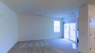 This single-floor space offers a clean, open layout designed for comfortable everyday living. The main living area is generously proportioned, featuring neutral wall-to-wall carpeting that provides a soft, understated foundation throughout the room. Crisp white walls and a smooth white ceiling contribute to a bright, airy atmosphere that feels open and inviting.

Natural light is a defining feature of this space. A large sliding glass door dominates one wall, allowing abundant light to pour in while also providing direct access to an outdoor area. Complementing this, a standard window on the adjacent wall further enhances the sense of openness and keeps the interior well-lit throughout the day.

The layout is straightforward and versatile, offering a blank canvas that can be adapted to a variety of furniture arrangements and uses. HVAC vents are integrated into the ceiling, ensuring consistent climate control throughout the space. The overall design is simple and functional, with a neutral color palette that lends itself well to a range of interior styles and décor preferences. The combination of ample natural light, open floor space, and clean finishes makes this a practical and welcoming environment.