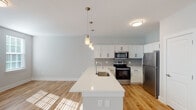 Located at 3818 Page Rd in Durham, NC, this single-floor residence offers a clean, contemporary design with thoughtful finishes throughout. The open-concept kitchen is a standout feature, showcasing white shaker cabinetry, a grey subway tile backsplash, stainless steel appliances including a range, microwave, and refrigerator, and a generous island with a white quartz countertop and undermount sink. Pendant lighting above the island adds a stylish touch, while warm hardwood-style flooring flows seamlessly into the living area, filling the space with natural light. The bedrooms are well-proportioned and finished with plush carpeting, neutral-toned walls, and windows fitted with blinds that allow for adjustable natural light. The hallway connects the living spaces to the private quarters with ease. Two bathrooms serve the unit: one features a walk-in shower with glass sliding doors and built-in shelving, while the second includes a full soaking tub and shower combination alongside a white vanity with a large mirror. Throughout the residence, a cohesive neutral color palette, crisp white trim, and quality finishes contribute to a bright, move-in-ready atmosphere that balances comfort and modern style.