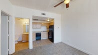 This single-floor residential unit offers a practical and comfortable layout designed for everyday living. The open living area is finished with plush carpeting and features a ceiling fan with a light fixture, creating a relaxed atmosphere. Clean white walls and textured ceilings contribute to a bright, airy feel throughout the space. The kitchen is accessible directly from the living area through an open archway, providing a seamless flow between the two spaces. It is equipped with light wood cabinetry offering ample storage, a double-basin stainless steel sink, a black dishwasher, and a black refrigerator, all set on easy-care hard surface flooring. The bedroom is generously sized with soft carpeting, a ceiling fan, and a large sliding glass window dressed with vertical blinds that allow natural light to fill the room. An adjacent closet provides convenient storage. The bathroom is neatly appointed with a combined tub and shower, a toilet, a single vanity sink with light wood cabinetry, a large mirror with overhead lighting, and hard surface flooring. The unit's neutral palette and functional design make it a well-rounded living space.