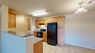 This single-story, 3-bedroom, 2-bathroom home offers a practical and efficient layout designed to maximize every square foot. The open-concept living and kitchen area serves as the heart of the home, featuring rich hardwood-style flooring, a ceiling fan with light fixture, and a front entry door flanked by a large window that invites natural light into the space. A dedicated tile entryway provides a clean transition from exterior to interior.

The kitchen is defined by warm honey-toned wood cabinetry with ample storage, granite-style countertops, a breakfast bar peninsula, and black appliances including an electric range and full-size refrigerator. A pendant light above the peninsula adds a touch of character to the cooking space.

The three bedrooms offer a mix of flooring options — some with plush carpeting and others with hardwood-style floors — providing versatility for different uses. The primary bedroom includes a dedicated closet outfitted with a wire shelving and hanging rod system. Each room is finished with neutral, warm-toned walls that create a calm and cohesive atmosphere throughout.

Both bathrooms feature tile flooring, warm wood vanities with granite-style counters, and clean, functional fixtures. A dedicated in-unit laundry area with wire shelving above adds everyday convenience to this well-appointed home.