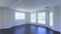 This single-floor space offers a clean, modern aesthetic defined by a thoughtful balance of light and form. The main living area is an open, airy room characterized by smooth, neutral-toned walls and crisp white trim that lend a fresh, understated elegance throughout. Underfoot, rich dark hardwood flooring provides a striking contrast to the light-filled surroundings, adding warmth and depth to the space.

Natural light is a defining feature, with multiple large windows fitted with horizontal blinds lining two walls of the main room. These windows frame views of lush green trees outside, creating a seamless visual connection to the natural environment and enhancing the sense of openness. The ceiling is smooth and well-proportioned, outfitted with recessed lighting and standard HVAC vents, contributing to a polished and functional finish.

The overall ambiance is calm and versatile, well-suited to a variety of uses. The combination of abundant natural light, quality flooring, and a neutral color palette creates an inviting and adaptable interior environment. The layout is straightforward and efficient, making the most of the available footprint while maintaining a sense of spaciousness throughout.