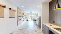 Located in Richmond, TX, this single-floor studio space is thoughtfully designed to serve as a modern craft and hobby room. The layout is efficient yet functional, making excellent use of every square foot available.

The kitchenette area is a standout feature, showcasing rich wood-tone cabinetry with brushed gold hardware, a sleek white countertop, and a deep undermount stainless steel sink with a matte black faucet. A built-in beverage refrigerator adds convenience, while two striking black pendant lights with gold interiors hang overhead, casting warm, focused light against a textured accent wall that adds depth and sophistication.

The main studio area is bright and open, anchored by a large window that floods the room with natural light and offers views of the surrounding community. A ceiling fan with integrated lighting keeps the space comfortable. A butcher block-top adjustable-height worktable with a matching stool serves as the central workspace. The full-length pegboard wall is outfitted with an organized array of tools and supplies, making it ideal for hands-on creative projects.

The space is finished with a patterned, distressed-style carpet tile flooring and crisp white walls adorned with bold framed wildlife artwork, giving the studio a contemporary, creative character. A glazed entry door with exterior visibility completes the welcoming atmosphere.