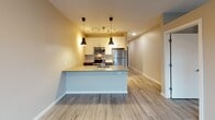 Located at 2323 NE Jackson St in Minneapolis, MN, this modern single-floor unit offers a thoughtfully designed open-concept layout that seamlessly connects the kitchen and living areas. The kitchen is a standout feature, equipped with stainless steel appliances including a refrigerator, electric range, and microwave. A central island with a double stainless steel sink and quartz-style countertops provides both workspace and casual dining potential. Dark cabinetry on the lower level contrasts with white upper cabinets, creating a contemporary two-tone aesthetic. Pendant lighting and a track light system illuminate the space with a warm, inviting glow. Light wood-style vinyl plank flooring runs throughout the unit, lending a clean and cohesive feel. The living area benefits from a large window fitted with a roller shade, allowing natural light to fill the room while offering views of the surrounding Minneapolis neighborhood. The bathroom is efficiently designed with tile-style flooring, a dark vanity with drawer storage, a wall-mounted grab bar, and clean white walls that maintain the unit's modern sensibility. The overall design is characterized by neutral tones, contemporary fixtures, and practical finishes that make for a comfortable and functional living environment.