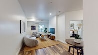 Located at 1120 S Walton Blvd in Bentonville, Arkansas, this single-floor unit offers a thoughtfully designed layout that combines comfort and modern style. The open-concept living area is anchored by warm wood-look flooring, recessed lighting, and bright white walls that create a clean, airy atmosphere. The living room provides generous space for seating arrangements and flows naturally into a dedicated dining nook, complete with a compact round table and bar-style stools. Natural light enters through large windows fitted with horizontal blinds, offering views of the surrounding neighborhood. The kitchen features a striking two-tone design, pairing white upper cabinetry with deep teal lower cabinets, all complemented by stainless steel appliances including a refrigerator, dishwasher, and range. The bedroom is a calm, well-proportioned retreat with plush carpeting, a sizable window, and a reach-in closet for ample storage. The bathroom includes warm stone-toned tile flooring, teal cabinetry, and a dedicated walk-in shower stall. Throughout the unit, the design aesthetic remains cohesive — neutral tones, clean lines, and modern finishes combine to create a welcoming and functional living environment suited for everyday comfort.