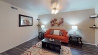 This single-floor residence offers a thoughtfully arranged layout that balances comfort and functionality across several distinct living areas. The living room sets a welcoming tone with rich hardwood-style flooring, a ceiling fan light fixture, and warm neutral walls that provide an inviting backdrop for relaxation. A dedicated dining area accommodates a round table with seating for four, accented by decorative wall art and matching dark hardwood-style flooring that continues throughout the main living spaces. The galley-style kitchen is efficiently designed with ample white cabinetry, generous counter space, a double-basin sink, and black appliances including a refrigerator and electric range. An overhead skylight-style fixture brightens the workspace, making it a practical and pleasant area for cooking. Both bedrooms feature plush carpeting, ceiling fan light fixtures, and natural light from windows dressed with teal curtains and white blinds. Each bedroom is complemented by a spacious reach-in closet with louvered bifold doors, providing excellent storage. The full bathroom is clean and functional, featuring a tiled tub-shower combination with a decorative curtain, toilet, and vanity. Throughout the residence, the cohesive design and warm color palette create a comfortable, move-in ready living environment.