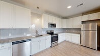 Located at 80 S 18th St. in Columbus, OH, this well-appointed 2-bedroom, 2-bathroom unit offers a thoughtfully designed single-floor layout with modern finishes throughout. The kitchen is a standout feature, showcasing crisp white shaker cabinets, granite-look countertops, a light gray subway tile backsplash, and a full suite of stainless steel appliances including a range, microwave, dishwasher, and refrigerator. Globe pendant lighting adds a contemporary touch above the workspace. Light wood-look flooring runs throughout the main living areas, creating a clean, cohesive aesthetic, while neutral walls in warm beige tones contribute to a bright and airy ambiance. The living room offers an open, flexible space with ample room for furnishings. Both bedrooms are carpeted for comfort, with the primary bedroom featuring a generous walk-in closet with wire shelving for organized storage. The bathrooms are finished with white cabinetry, granite countertops, and wood-look tile flooring; one includes a glass-enclosed walk-in shower with natural light from a window. A dedicated laundry area houses a stacked washer and dryer unit for added convenience. A connecting hallway ties the layout together efficiently, making this a functional and attractive home.