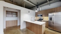 Located at 15907 Ash Way in Lynnwood, WA, this one-bedroom, one-bathroom unit showcases a compelling industrial-modern aesthetic throughout its efficiently designed single floor. Polished concrete floors and exposed ceiling ductwork and piping lend the space a loft-like character, while pendant lighting adds warmth and definition to key areas.

The open-concept layout seamlessly connects the kitchen, dining, and living areas. The kitchen is a standout feature, equipped with warm wood-grain cabinetry extending to the ceiling for ample storage, a stainless steel appliance suite including a French door refrigerator, electric range, and built-in microwave, a subway tile backsplash, and a generous island with a white quartz countertop and undermount sink. Large floor-to-ceiling windows and a glass-panel door in the living area flood the space with natural light and provide outdoor views, complemented by a ceiling fan overhead.

The bedroom offers a private retreat with two closets, including a walk-in with built-in shelving. The bathroom and laundry room are combined, featuring a glass-enclosed tile shower, toilet, and in-unit laundry access. A hallway connects the living spaces to the private quarters, completing this thoughtfully laid-out urban home.
