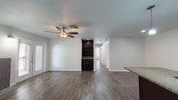This single-floor residence offers a cohesive and thoughtfully designed layout with consistent finishes throughout. Rich, dark hardwood-style flooring runs continuously across all rooms, anchoring the space with a warm and unified aesthetic.

The kitchen is a standout feature, equipped with dark espresso cabinetry, granite countertops, stainless steel appliances including a range, microwave, and refrigerator, and a central island with a built-in sink and pendant lighting overhead. Track lighting and recessed fixtures provide ample illumination, while a tiled backsplash adds a refined detail.

The open living and dining area flows naturally from the kitchen, highlighted by a ceiling fan with light fixture and a built-in shelving unit with dark cabinetry below — a practical and stylish addition. The space connects to a hallway leading to the remaining rooms.

The bedrooms are generously sized, each featuring ceiling fans, large windows fitted with horizontal blinds that invite natural light, and the same durable hardwood-style flooring found throughout the residence.

The bathroom includes a full tub-and-shower combination clad in neutral-toned subway tile with a decorative mosaic border accent, brushed nickel fixtures, and clean white finishes that lend a polished, contemporary feel to the space.