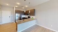 Located at 2120 N Brevard St in Charlotte, NC, this one-bedroom, one-bathroom apartment offers a well-designed single-floor layout that maximizes its cozy footprint. The open-concept living and kitchen area is anchored by a peninsula with granite countertops, providing ample prep space and a casual dining option. The kitchen is outfitted with rich dark cabinetry, a full suite of stainless steel appliances including a French door refrigerator, electric range, and built-in microwave, as well as light wood-style flooring that extends throughout the main living area. Stylish pendant lights illuminate the peninsula, adding a contemporary touch to the space. The bedroom is a comfortable retreat featuring plush carpeting, a ceiling fan, and a window fitted with blinds that allows for natural light and views of the surrounding area. Multiple closet doors offer convenient storage. The bathroom is thoughtfully finished with subway tile surrounding the full soaking tub and shower, light wood-look tile flooring, a dark vanity with granite countertops, and built-in open shelving for storage. Neutral gray walls throughout the unit create a clean, modern aesthetic. This apartment is ideal for those seeking a stylish and functional home in Charlotte.