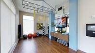 Located at 1000 Antietam Creek Dr in Fayetteville, NC, this single-floor fitness studio is thoughtfully designed to support a wide range of workout styles and training routines. The space features rich hardwood flooring that provides both durability and a polished aesthetic, while the open layout offers ample room for movement and group activities. A prominent overhead metal training rig spans the ceiling, complete with hanging aerial straps and resistance bands, making it ideal for suspension and aerial fitness training. Natural light filters in through large windows, brightening the room and creating an energizing workout atmosphere. A large wall-mounted flat-screen display is positioned at the front of the space, enabling guided fitness classes and on-demand workout programming. The studio is well-equipped with a variety of exercise tools, including stability balls, medicine balls, and step platforms, all neatly organized for easy access. Accent blue walls and ceiling fans add to the clean, modern aesthetic of the space. Full-length mirrors along one wall enhance the sense of openness while allowing users to monitor their form during training. This fitness studio combines functional design with a welcoming environment, making it a versatile space suited for individual training sessions and group fitness classes alike.