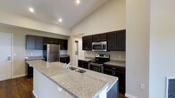 This single-floor, two-bedroom, two-bathroom residence offers a thoughtfully designed layout that maximizes both functionality and comfort. The kitchen serves as a standout feature, showcasing dark espresso cabinetry that contrasts elegantly with granite-style countertops. A large kitchen island with an integrated sink provides ample workspace and doubles as a casual dining or entertaining area. Stainless steel appliances, including a refrigerator, electric range, and built-in microwave, complete the modern kitchen setup. Vaulted ceilings in the kitchen and adjoining areas lend a sense of openness and airiness to the space, enhanced by recessed lighting that ensures consistent illumination throughout. The neutral wall tones complement the rich cabinetry, creating a cohesive and inviting atmosphere. The open-concept design encourages a natural flow between the kitchen and living areas. With two well-proportioned bedrooms and two full bathrooms, this residence provides comfortable, practical accommodations suitable for a variety of lifestyles.
