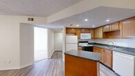 Located at 6650 Creek Bay Dr in Indianapolis, IN, this single-floor, one-bedroom, one-bathroom unit offers a functional and well-organized layout. The open-concept living area seamlessly connects the kitchen, dining, and living spaces, all finished with durable hardwood-style flooring. The kitchen is a standout feature, equipped with warm-toned wood cabinetry, dark granite-style countertops, a central island with additional counter space, recessed lighting, and white appliances including a refrigerator, range, microwave, and dishwasher. A pendant light fixture highlights the dining area, while a ceiling fan adds comfort to the living space. The bedroom features plush wall-to-wall carpeting, a natural light window with blinds, and access to a closet. The full bathroom includes a tiled tub-shower combination, a vanity with matching cabinetry, and hardwood-style flooring. Additional conveniences include three closets, an in-unit laundry area, and a utility room. Textured ceilings are present throughout, and a sliding door off the main living area provides access to an outdoor space, bringing in natural light.