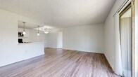 Located at 5300 Cinderlane Parkway in Orlando, Florida, this 2-bedroom, 2-bathroom single-floor residence offers a well-organized layout with a clean, modern aesthetic throughout. The open living area features light wood-look flooring and a textured ceiling, seamlessly connecting to the kitchen via a peninsula counter with pendant lighting overhead. The kitchen is outfitted with white upper cabinetry, warm wood-toned lower cabinets, white countertops, and stainless steel appliances including a refrigerator, range, and over-the-range microwave, all set on matching wood-look flooring. The primary bedroom is a comfortable, well-proportioned room with wood-look flooring, a large window inviting generous natural light, and direct sliding glass door access to an outdoor balcony with exterior views. The second bedroom also features wood-look flooring and a bright window overlooking the outdoor surroundings. Both bathrooms are finished with neutral tile flooring and light wood-toned cabinetry. One bathroom includes a soaking tub with tiled surround and a decorative mosaic accent border, while the second bathroom features a broad vanity with a speckled stone-look countertop and a large mirror. The unit is completed by a hallway and a closet for additional storage.