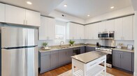 This well-appointed three-story home offers a smart, modern layout distributed across three distinct levels. The ground floor provides convenient access through an attached garage with an automatic door opener, alongside an entry hallway finished with warm hardwood flooring and carpeted stairs leading to the main living areas.

The main level serves as the social heart of the home, featuring an open-plan kitchen and living room bathed in natural light from large windows with plantation shutters. The kitchen is a standout, showcasing two-tone cabinetry—white uppers and slate-gray lowers—paired with neutral quartz countertops, stainless steel appliances including a gas range and built-in microwave, and a movable kitchen island. The adjacent living room offers a relaxed, airy atmosphere with recessed lighting, hardwood flooring, and direct access to an outdoor area through glass-paneled doors. Three well-appointed bathrooms are distributed throughout the home, each featuring neutral stone countertops, undermount sinks, and gray vanity cabinetry.

The upper level hosts the spacious primary bedroom, filled with natural light through oversized windows and outfitted with plush carpet. A dedicated office with a closet and carpet flooring provides a quiet workspace. The clean, neutral palette and contemporary finishes throughout create a cohesive and inviting atmosphere ideal for modern living.