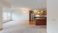 This single-floor, one-bedroom, one-bathroom unit is thoughtfully designed to maximize functionality and comfort. The open-concept layout seamlessly connects the kitchen and living area, creating a cohesive and inviting space. The kitchen is a standout feature, showcasing warm-toned wood cabinetry extending to the ceiling for ample storage, granite-style dark countertops, and a breakfast bar island ideal for casual dining or meal prep. Stainless steel appliances, including a refrigerator, range, and built-in microwave, complete the kitchen. Hardwood flooring anchors the kitchen area, transitioning to plush carpeting throughout the living room and bedroom.

The spacious living room benefits from abundant natural light through large windows and a sliding glass door that opens to a private balcony, offering outdoor views. The bedroom is generously sized, featuring a large window with exterior views and convenient access to both a walk-in closet and in-unit laundry.

The bathroom is well-equipped, offering both a soaking tub with tile surround and a separate glass-enclosed shower stall, along with a pedestal sink and tile flooring. The overall ambiance is clean, neutral, and move-in ready.