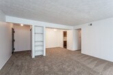 This single-floor residence offers a practical and comfortable layout designed for everyday living. The main living area is generously proportioned, featuring wall-to-wall beige carpeting and a textured ceiling that adds a classic touch. A built-in shelving unit divides the space, providing both storage and visual interest, while a large sliding glass door dressed with vertical blinds fills the room with natural light and offers access to the outdoors. The open floor plan allows the living space to flow seamlessly into adjacent areas, creating a sense of connectivity throughout.

The kitchen is efficiently laid out with dark wood cabinetry — both upper and lower — paired with light-toned countertops that include a double-basin sink. Dark hardwood-style flooring grounds the space and contrasts cleanly with the white gas range. A built-in dishwasher adds a practical convenience to the well-organized galley-style kitchen.

The bathroom is neatly appointed with dark hardwood-style flooring that mirrors the kitchen, a vanity featuring a marble-toned countertop and an undermount sink, and a full tub-shower combination enclosed by sliding glass doors. The overall ambiance of the space is clean, neutral, and move-in ready, offering a solid foundation for personalization.