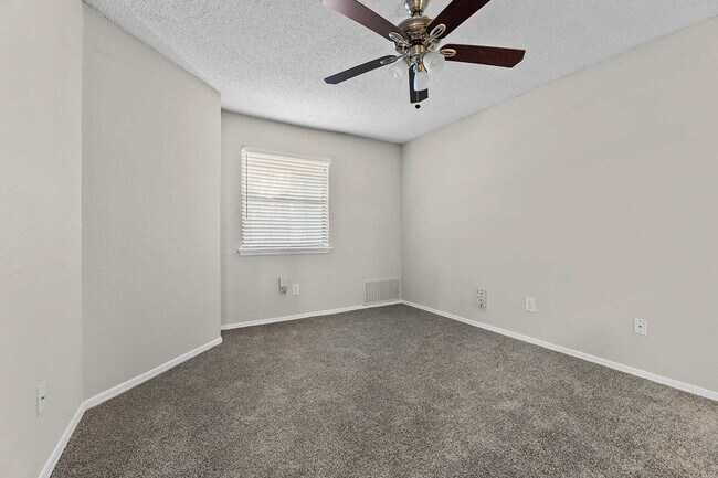 Habitación vacía con moqueta gris, ventilador de techo con luz, ventana con persianas y techo texturizado. - Walnut Creek at 122