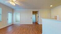 Located at 50 Lily Green Ct NW in Concord, NC, this single-floor home offers a well-organized layout with a clean, functional design throughout. The main living area is appointed with warm hardwood-style flooring, crown molding, and a ceiling fan with light fixture, creating a bright and welcoming atmosphere. A door leads directly to an outdoor area, allowing natural light to fill the space. The living area flows seamlessly into the kitchen via a breakfast bar peninsula. The kitchen features white cabinetry with ample storage, light countertops, a full suite of white appliances including a refrigerator, electric range, and dishwasher, all set atop matching hardwood-style flooring. The bedrooms are carpeted and generously sized, each featuring large windows fitted with blinds that invite natural light and offer views of the surrounding landscape. The bathroom is finished with hardwood-style flooring, a white vanity with a large mirror, a tub-shower combination accented with decorative tile detailing, and accessibility grab bars. Crown molding and consistent neutral tones carry throughout the home, contributing to a cohesive and comfortable living environment.