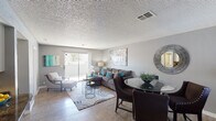 This single-floor residence presents a thoughtfully designed layout that balances open communal spaces with comfortable private retreats. The living and dining area forms the heart of the home, featuring wood-look flooring, a textured ceiling, and neutral gray walls that provide a versatile backdrop. A sliding glass door floods the living space with natural light and provides access to an outdoor balcony area. The dining space accommodates a glass-top table, while the living area offers ample room for generous seating arrangements.

The kitchen is equipped with white cabinetry, dark granite-style countertops, black appliances including a refrigerator, electric range, and dishwasher, and a recessed ceiling fixture that adds warmth. A convenient breakfast bar connects the kitchen to the main living area.

Two bedrooms feature plush carpeting, gray walls, and textured ceilings. The primary bedroom includes a mirrored sliding-door closet, while the secondary bedroom also offers dedicated closet storage. Both rooms are well-proportioned and receive natural light.

Two bathrooms serve the residence—one featuring a walk-in shower and the other a full tub-shower combination—each with wood-look flooring and clean white fixtures.