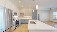 This thoughtfully designed residence offers three bedrooms, two bathrooms, and a seamless single-floor layout that maximizes both comfort and functionality. Light-toned hardwood flooring runs throughout the main living areas and bedrooms, creating a cohesive and airy feel. The open-concept kitchen is a standout feature, boasting two-tone shaker cabinetry in white and soft gray, a striking marble-inspired tile backsplash, quartz countertops, stainless steel appliances, and an oversized island with pendant lighting — ideal for both cooking and casual dining. The kitchen flows naturally into the bright living area, which is anchored by large windows and a glass door that invite abundant natural light and outdoor views. A ceiling fan adds comfort to the living space. The primary bedroom is generously proportioned and connects to a well-appointed en-suite bathroom featuring a wide quartz vanity, light wood cabinetry, and access to a dedicated walk-in closet. The second bathroom includes a full tub-shower combo with marble-style tile surround and built-in shelving. The two additional bedrooms are bright and versatile, each featuring hardwood floors and windows with exterior views. A convenient in-unit washer and dryer area is tucked neatly within the layout, adding everyday practicality to this modern residence.