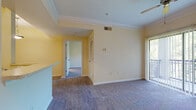 This single-floor residence offers a thoughtfully designed layout that balances comfort and functionality throughout. The living area is generously sized, featuring soft carpeting, crown molding, and a ceiling fan, with a large sliding glass door that opens to a private balcony overlooking lush greenery, filling the space with natural light.

The kitchen is accessed via an arched passageway and features warm wood cabinetry, black appliances including a refrigerator, electric range, and built-in microwave, as well as light tile flooring. A peninsula counter with a pendant light above connects the kitchen to the living and dining areas, making it ideal for both everyday use and entertaining.

The bedrooms are carpeted and bright, with neutral walls and windows that invite natural light. One bedroom includes a walk-in closet with a built-in hanging rod, while an additional electrical panel is conveniently located nearby. The bathroom is well-appointed with warm wood vanity cabinetry, a tiled tub-and-shower combination, a large mirror, and tile flooring throughout.

Crown molding and consistent warm, neutral tones throughout the living spaces create a cohesive and inviting ambiance. The overall layout is efficient and practical, offering comfortable living across every room.