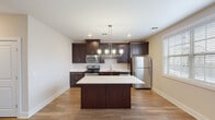 Located at 145 Monmouth St in the heart of Red Bank, NJ, this single-floor unit offers a thoughtfully designed layout with modern finishes throughout. The kitchen is a standout feature, showcasing rich dark espresso cabinetry reaching toward the ceiling, crisp white countertops, and a full suite of stainless steel appliances including a gas range, built-in microwave, dishwasher, and refrigerator. A center island provides additional prep space and casual seating, while a sleek pendant chandelier adds a refined touch overhead. Warm hardwood-style flooring runs throughout the main living areas, lending continuity and a welcoming ambiance. The living space is open and bright, with clean white walls and a neutral palette that maximizes the sense of openness. The bedrooms are well-sized, each featuring natural light from windows with blinds; one room features hardwood-style flooring while another is finished with plush carpet for added comfort. The bathroom is cleanly appointed with a tiled tub-and-shower combination with glass sliding doors, a dark-cabinetry vanity with a white countertop, and wood-look tile flooring. The overall design balances contemporary style with functional living in a prime Red Bank location.
