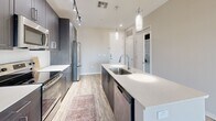 Located at 4949 N 7th St in Phoenix, Arizona, this well-appointed one-bedroom, one-bathroom unit offers a thoughtfully designed layout with modern finishes throughout. The open-concept kitchen serves as the heart of the space, featuring a large center island with a white quartz countertop and an undermount sink, dark espresso cabinetry extending to the ceiling for ample storage, and a full suite of stainless steel appliances including a French door refrigerator, electric range, microwave, and dishwasher. Pendant lighting and track lighting illuminate the kitchen, which flows seamlessly into the living area. Light wood-look flooring runs through the main living spaces, adding warmth and continuity. A sliding glass door leads to a private balcony, allowing natural light to fill the living area. The bedroom is comfortably sized with plush carpet flooring, a ceiling fan, and a window offering exterior views. The bathroom features wood-look tile flooring, a dark-toned vanity with a white countertop, a soaking tub, and direct access to a dedicated walk-in closet with built-in shelving. An in-unit washer and dryer area is also included, adding everyday convenience to this clean, contemporary Phoenix residence.