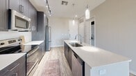 Located at 4949 N 7th St in Phoenix, Arizona, this well-appointed one-bedroom, one-bathroom unit offers a thoughtfully designed layout with modern finishes throughout. The open-concept kitchen serves as the heart of the space, featuring a large center island with a white quartz countertop and an undermount sink, dark espresso cabinetry extending to the ceiling for ample storage, and a full suite of stainless steel appliances including a French door refrigerator, electric range, microwave, and dishwasher. Pendant lighting and track lighting illuminate the kitchen, which flows seamlessly into the living area. Light wood-look flooring runs through the main living spaces, adding warmth and continuity. A sliding glass door leads to a private balcony, allowing natural light to fill the living area. The bedroom is comfortably sized with plush carpet flooring, a ceiling fan, and a window offering exterior views. The bathroom features wood-look tile flooring, a dark-toned vanity with a white countertop, a soaking tub, and direct access to a dedicated walk-in closet with built-in shelving. An in-unit washer and dryer area is also included, adding everyday convenience to this clean, contemporary Phoenix residence.
